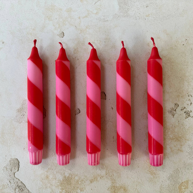 Five red and pink striped candles on a textured surface