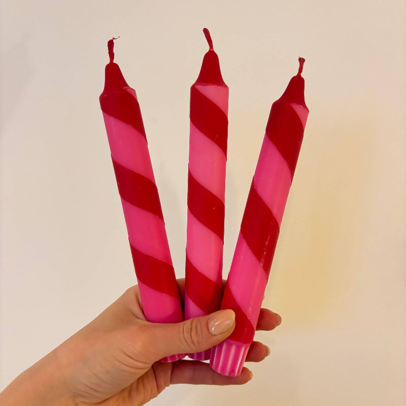 Three red and pink striped candles held by a hand against a light background