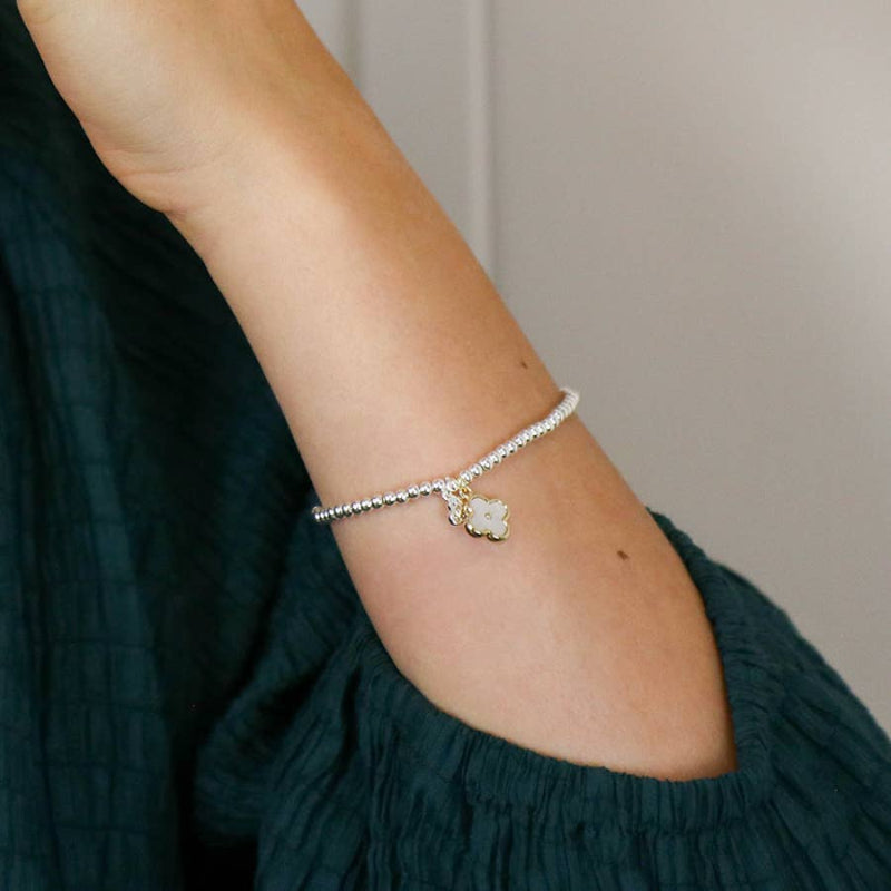 Silver bracelet with a small charm on a person's wrist against a neutral background