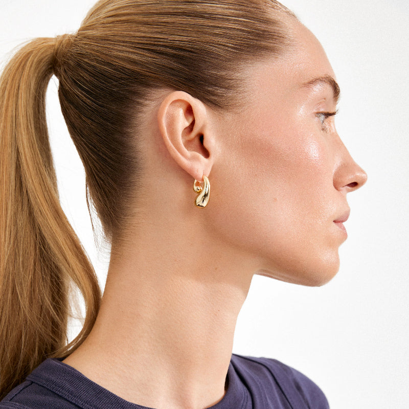 Close-up of a woman wearing a gold earring with a plain background