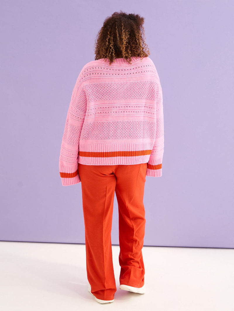 Person wearing a pink sweater and red pants against a purple background