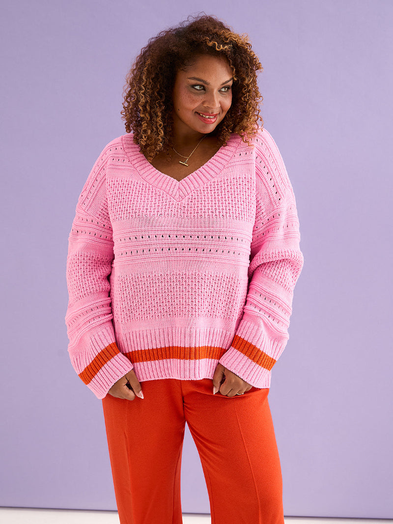 Woman wearing a pink sweater with orange accents against a purple background