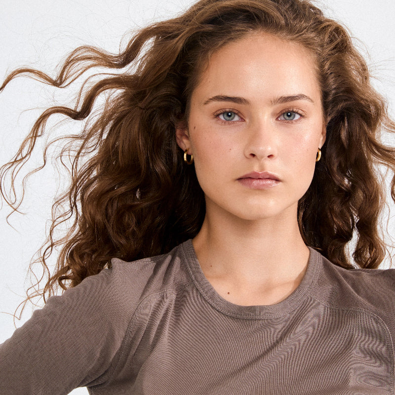 Woman with wavy brown hair wearing a brown shirt against a white background