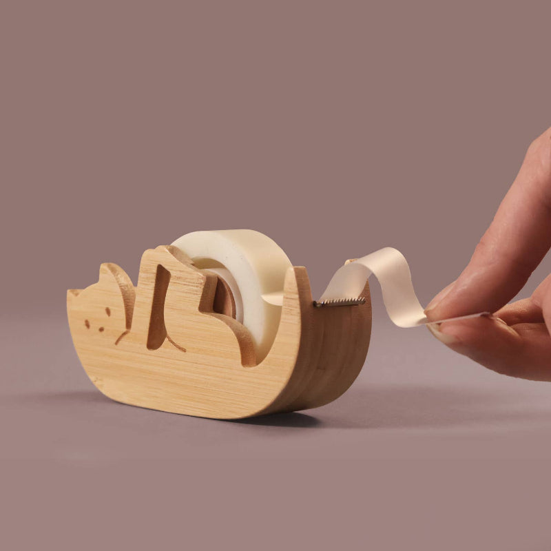 Wooden  Kitty Sticky Tape Dispenser with a hand pulling tape from it on a brown background