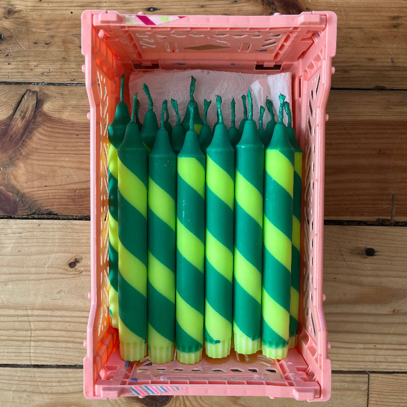 Green and yellow striped candles in a pink crate on a wooden surface