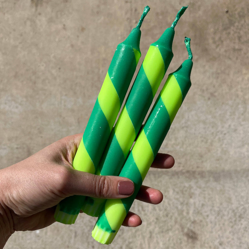 Hand holding three green and yellow striped candles against a concrete background