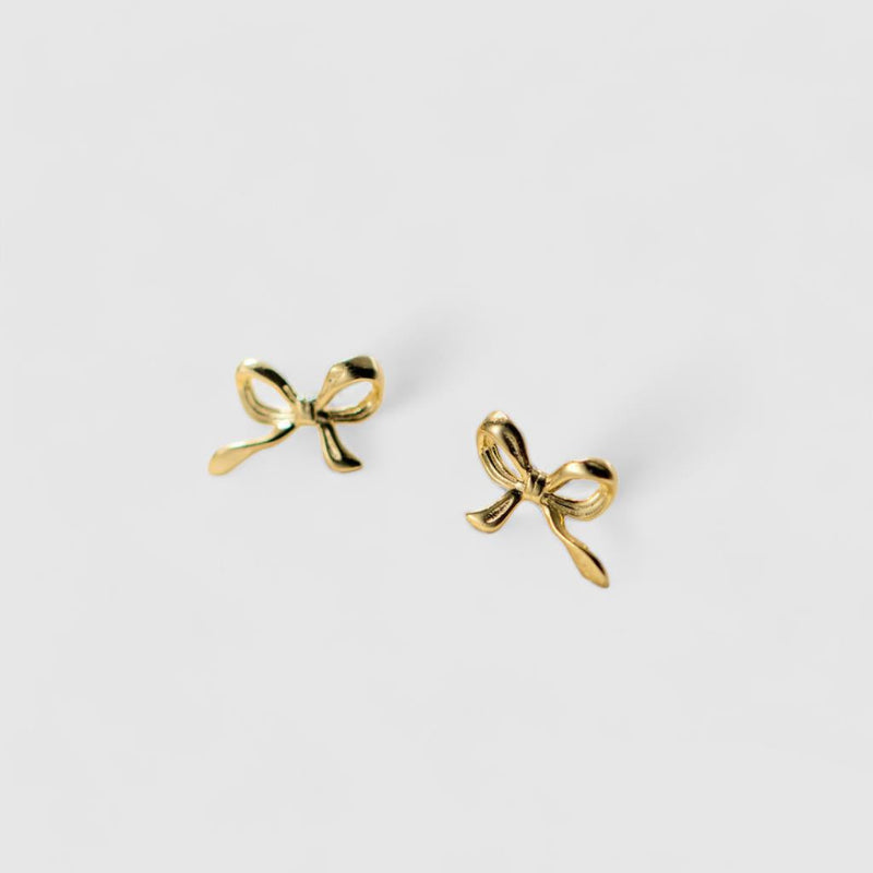Gold bow-shaped earrings on a light gray background