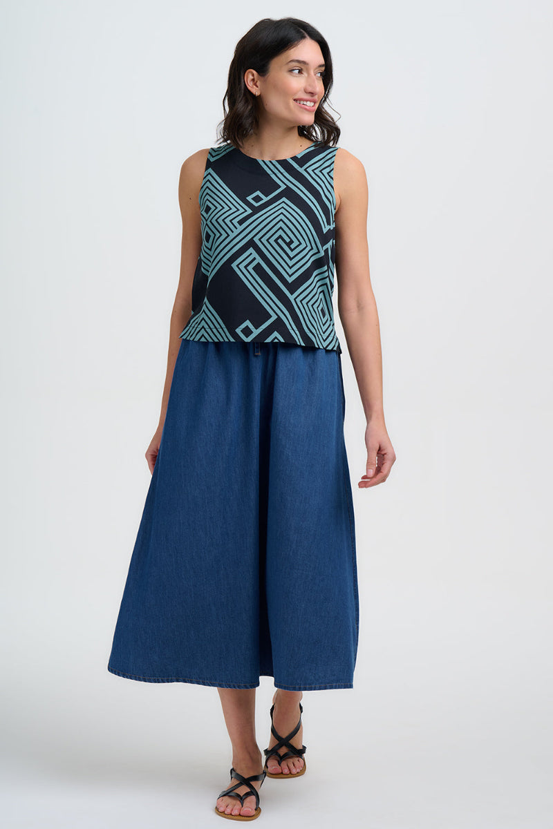 Woman wearing a sleeveless top with geometric pattern and a long blue skirt on a white background