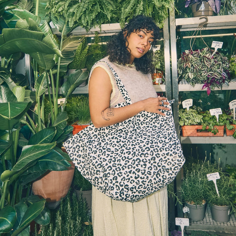 Woman holding a leopard print Roka Marylebone large tote bag in a plant store