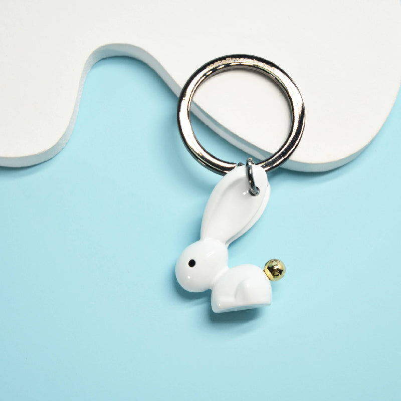 White ceramic keychain shaped like wireless earbuds on a light blue background