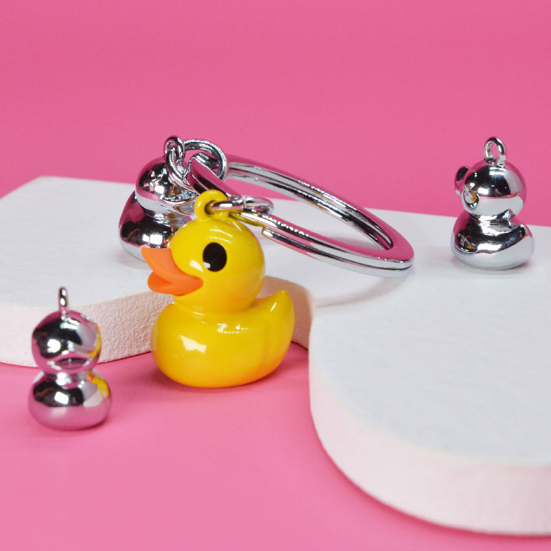 Yellow rubber duck keychain with silver ducks on a pink background