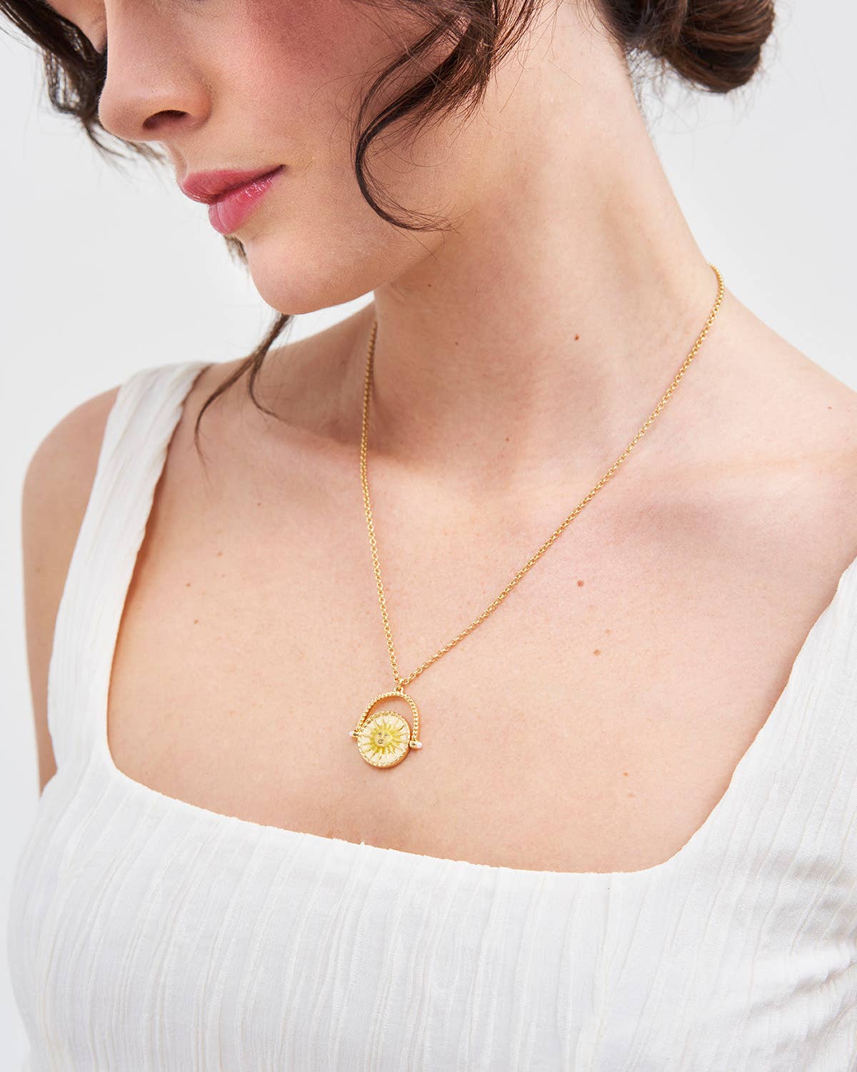 Woman wearing a gold necklace with a circular pendant on a plain background