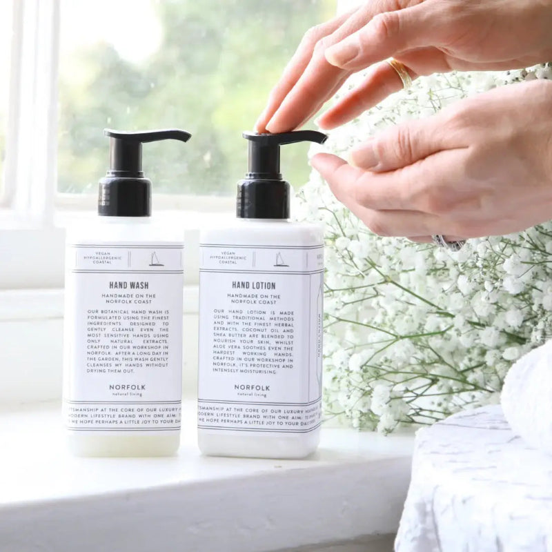 Hand wash and hand lotion bottles with a person applying lotion, set against a blurred natural background.