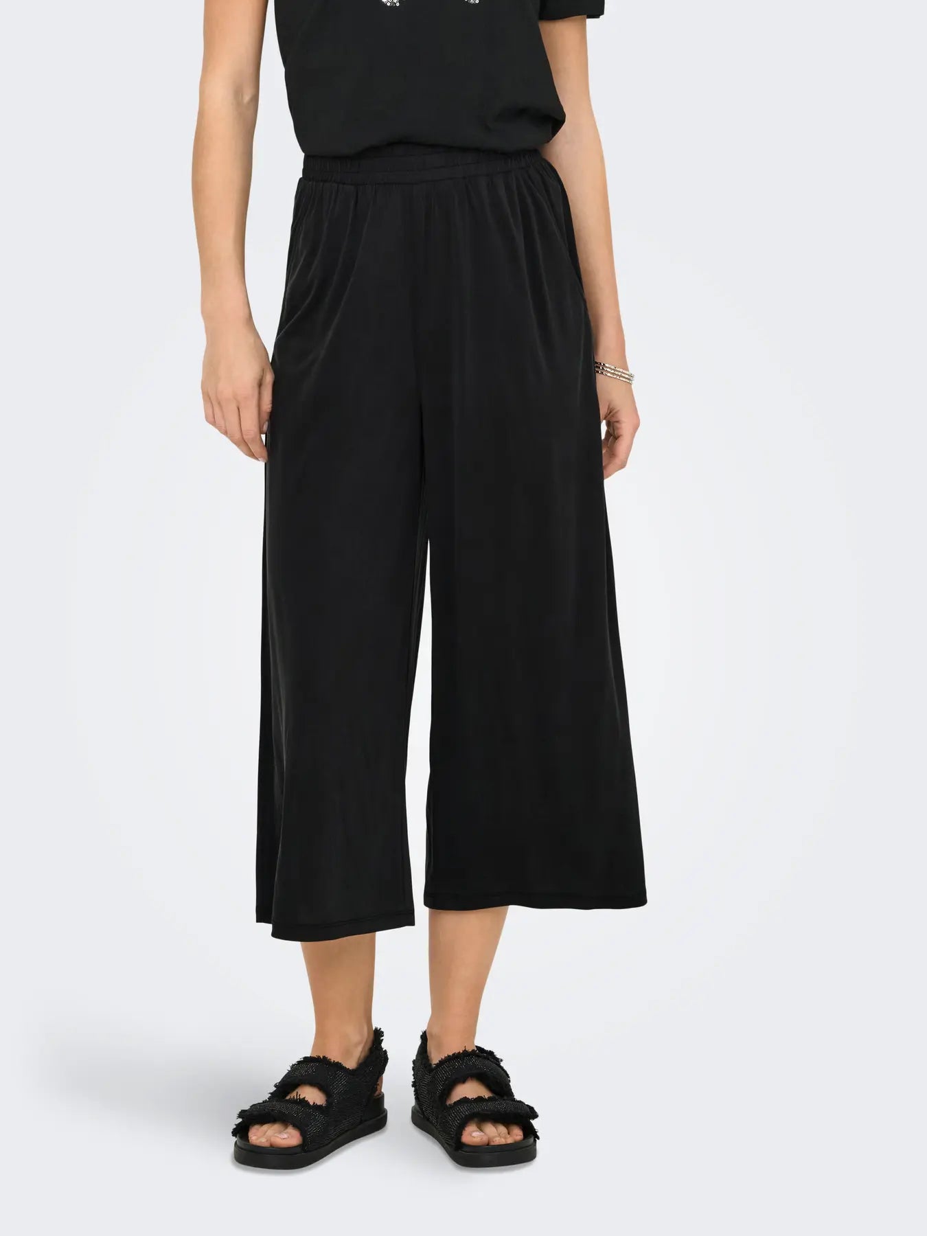 Person wearing black wide-leg pants and sandals on a white background