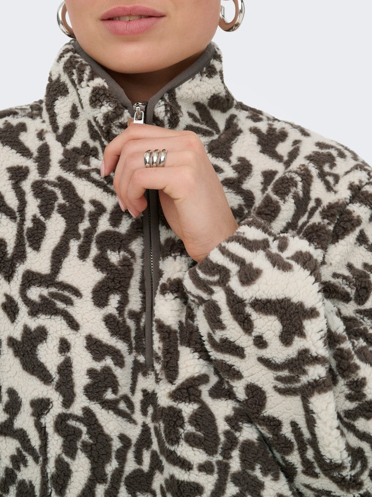 Close-up of a person wearing a plush fleece quarter-zip jacket with a brown and cream animal print pattern, holding the zipper tab with one hand.