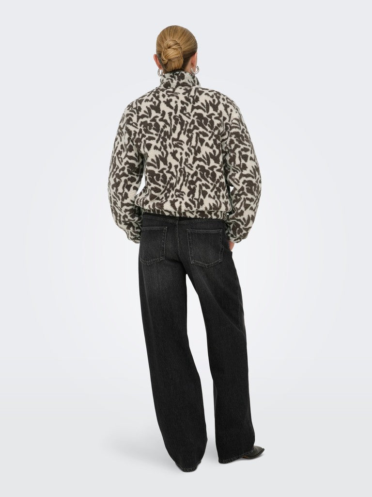 A model viewed from behind wearing a cropped, long-sleeve jacket with an abstract black and beige pattern, paired with black wide-leg jeans, against a light gray studio background.