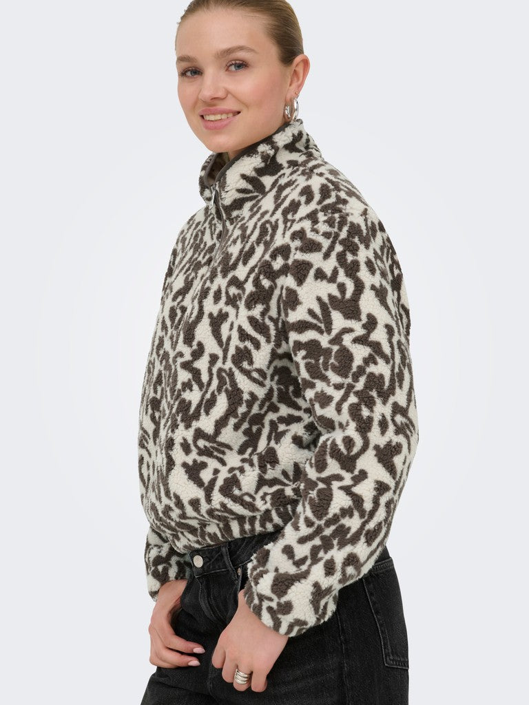 A woman wearing a fuzzy long-sleeve fleece pullover with a brown and beige animal print pattern, paired with black jeans, shown against a plain light gray background.