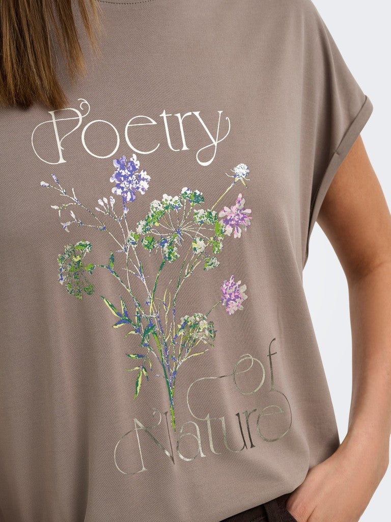 A close-up of a person wearing a taupe-brown t-shirt with a graphic print that reads 'Poetry of Nature' in white and green script, decorated with a central illustration of wildflowers in purple, green, and white.