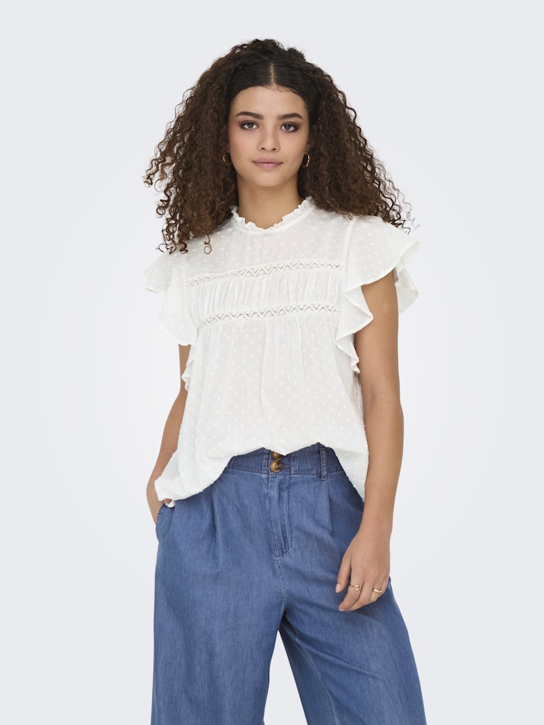 Woman wearing a white blouse with ruffled details and blue pants on a white background