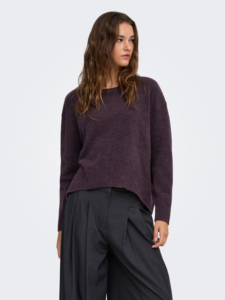 A woman wearing a dark plum purple knit sweater and dark charcoal gray wide-leg trousers, photographed against a clean light gray studio background.
