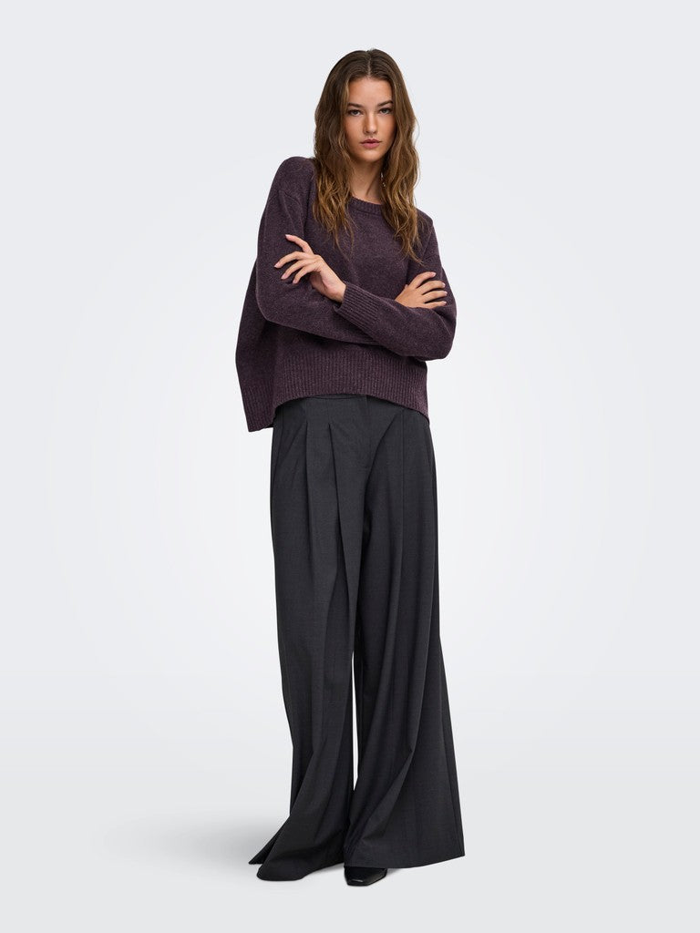 A woman modeling a dark plum purple knit sweater and wide-leg charcoal gray trousers against a light gray studio background.