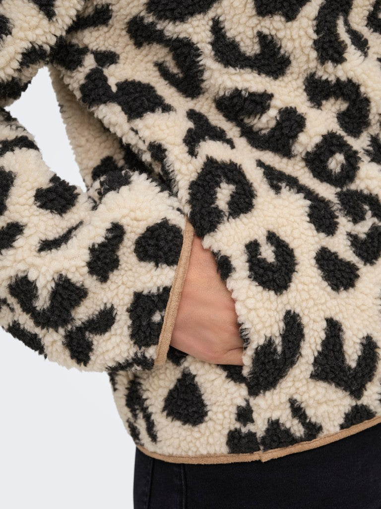 Close-up of a cream sherpa fleece jacket with a black leopard print pattern and a side pocket showing a hand inside, paired with dark pants.
