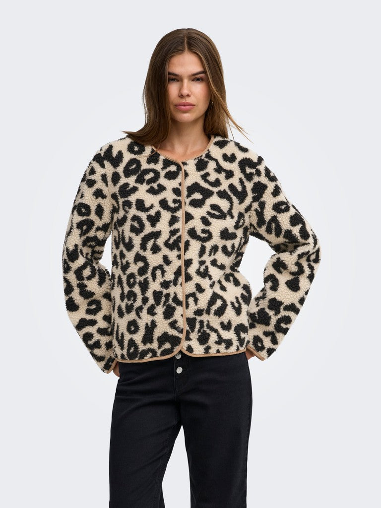 A woman modeling a fuzzy leopard-print jacket with black pants against a light gray studio background.