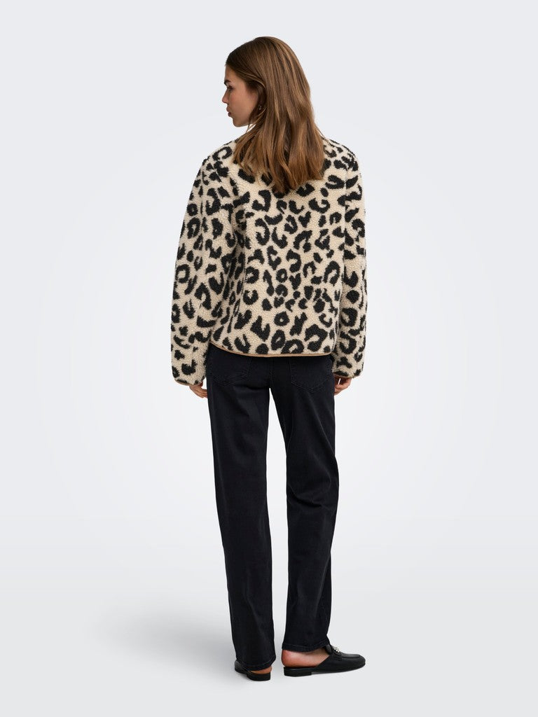 A woman shown from the back wearing a beige faux-fur jacket with a black leopard print pattern, paired with black trousers and black flat shoes, against a light gray studio background.