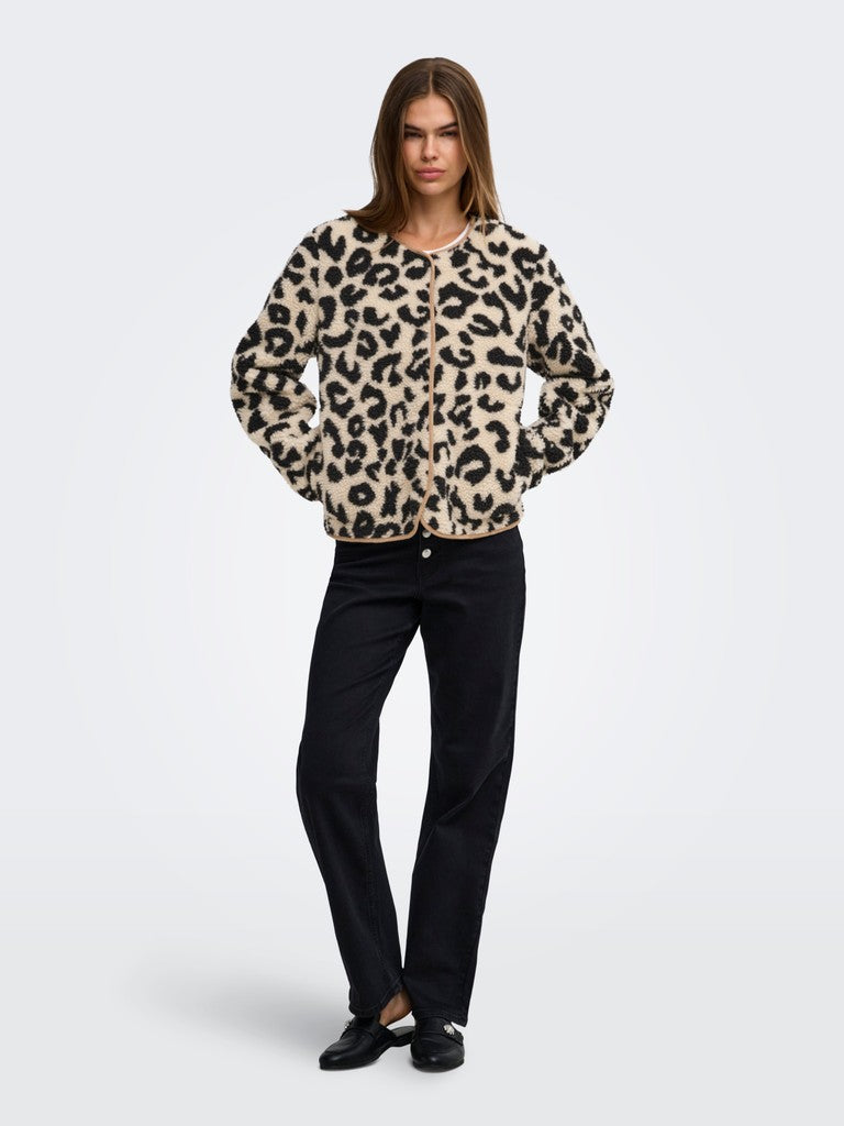 A woman modeling a beige and black leopard-print fuzzy cardigan with black pants, standing against a light gray studio background.