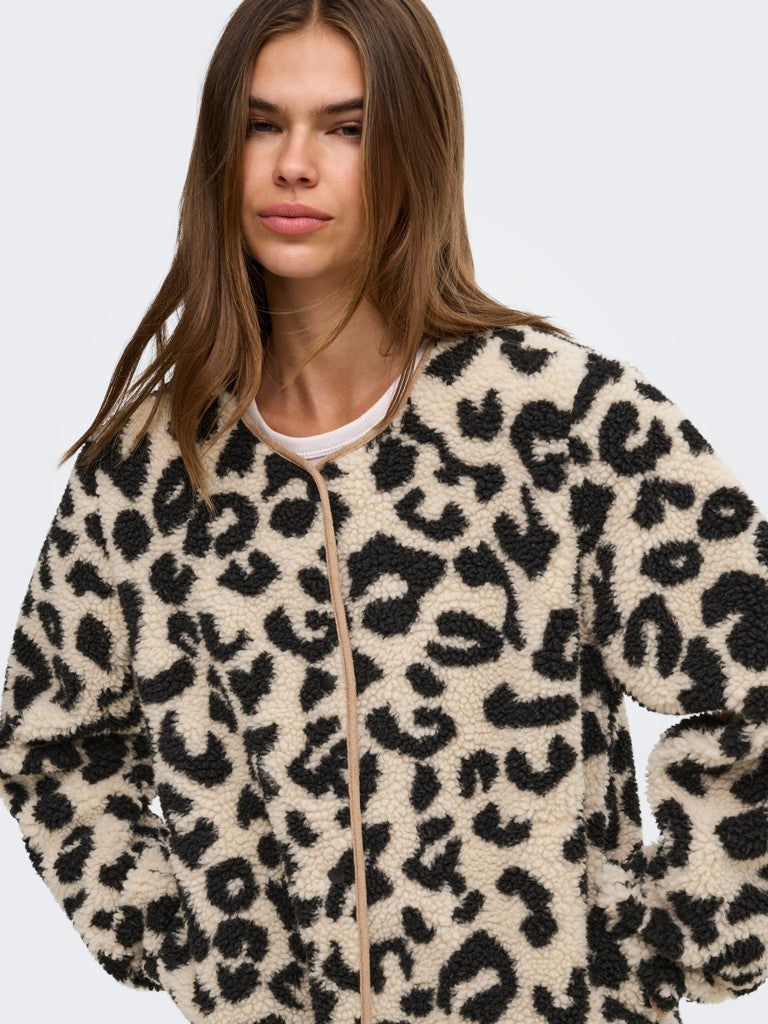 A woman wearing a plush leopard-print fleece zip-up jacket over a white crewneck shirt, photographed against a light gray studio background.