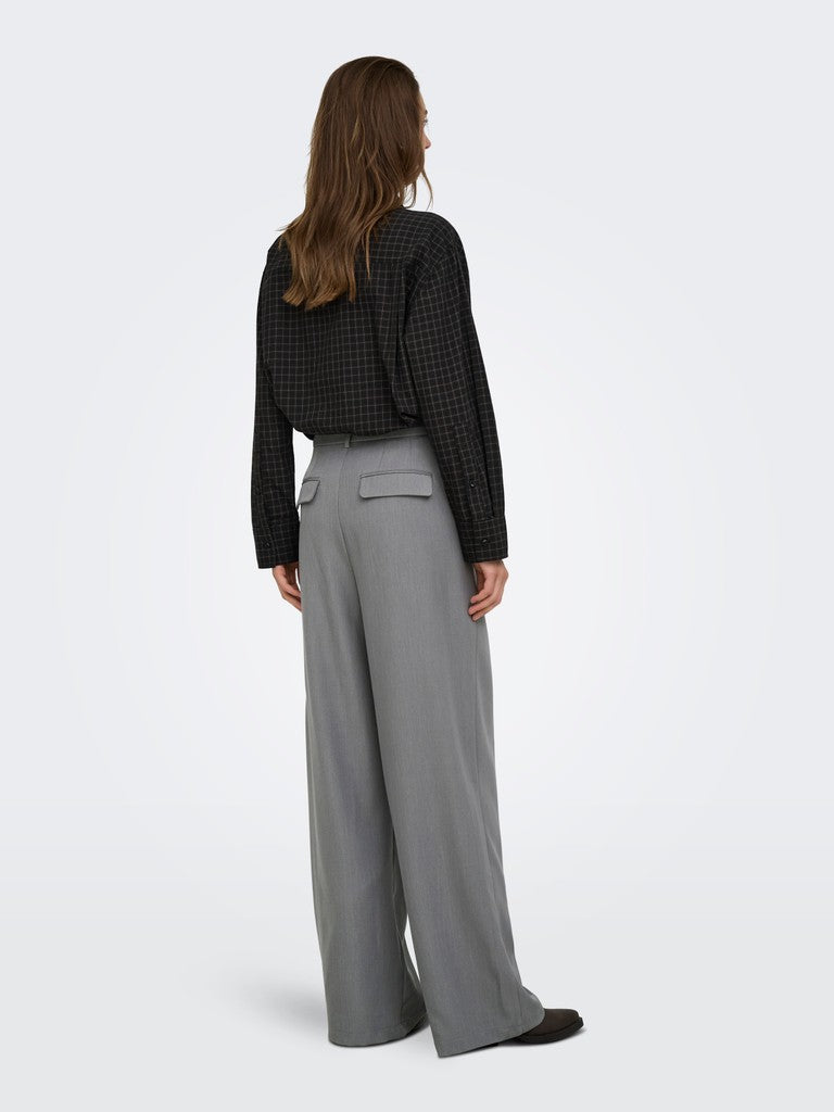 A woman shown from the back wearing a black patterned long-sleeve top and high-waisted gray wide-leg trousers, photographed against a clean light gray studio background.