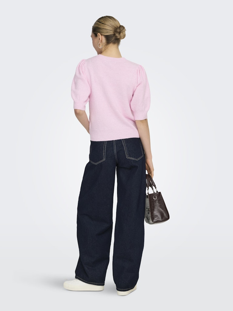 Person wearing a pink sweater and dark blue jeans holding a brown handbag on a white background