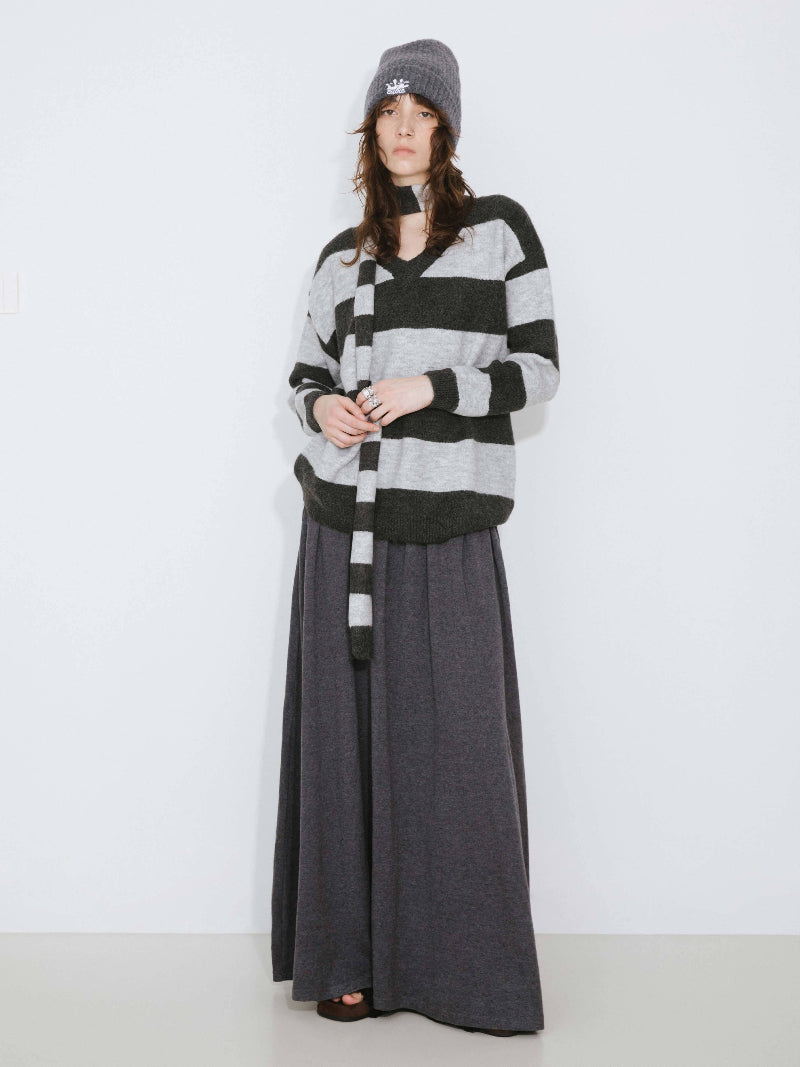Woman wearing a black and gray striped sweater with a long gray skirt on a white background