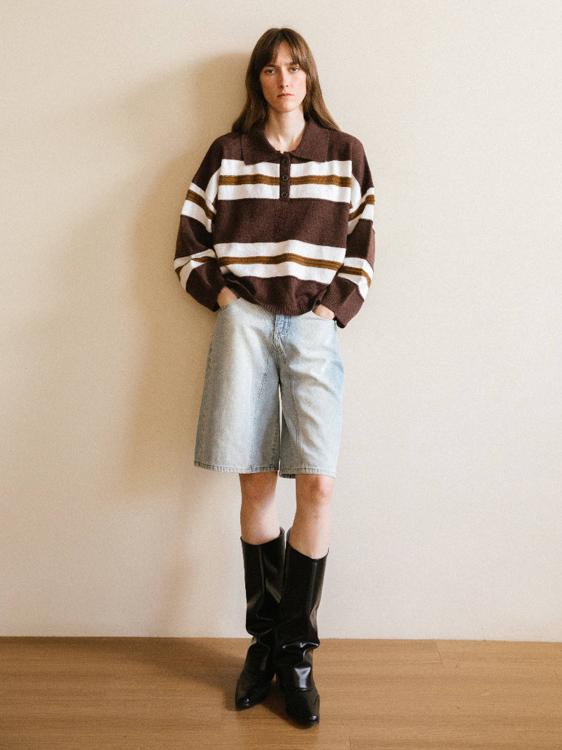 Person wearing a brown and white striped sweater, light blue shorts, and black boots against a plain wall.