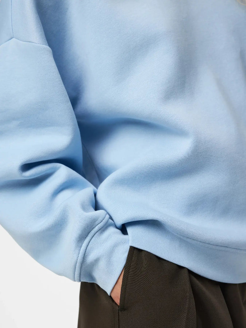 Close-up of a person wearing a light blue sweatshirt with dark brown pants, showing the fabric texture and cuff detail.