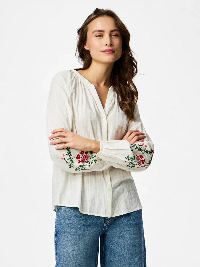 Woman wearing a white blouse with floral embroidery on a white background