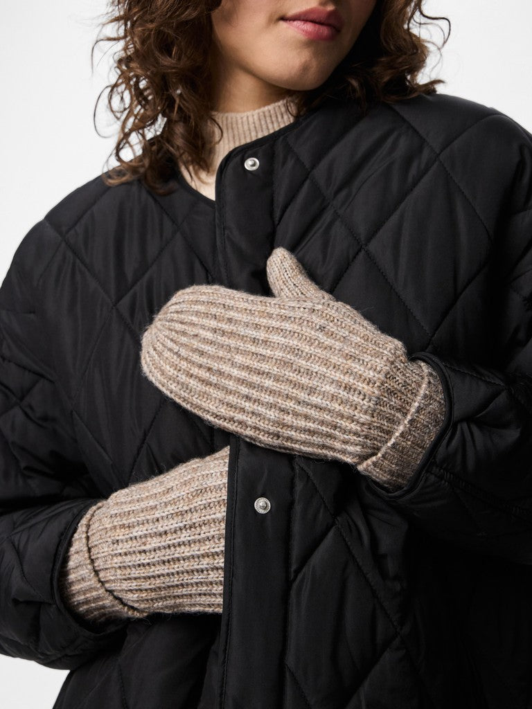 Person wearing black quilted jacket and beige knitted mittens on a plain background