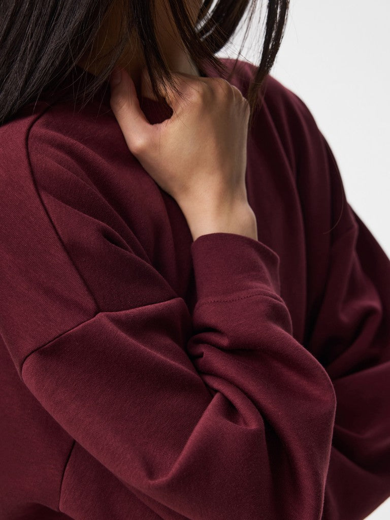 Close-up of a person wearing an oversized burgundy sweatshirt, showing the soft texture of the fabric and the relaxed fit against a plain light background.