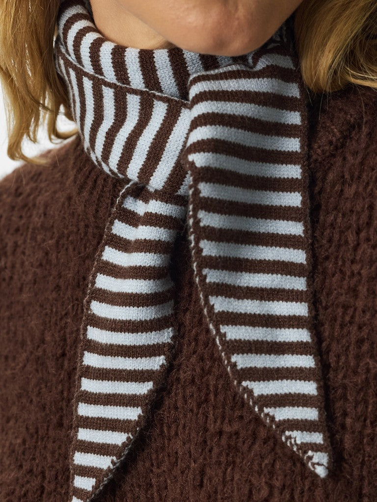 A close-up of a person wearing a brown and white striped knit scarf tied around the neck over a brown textured sweater.
