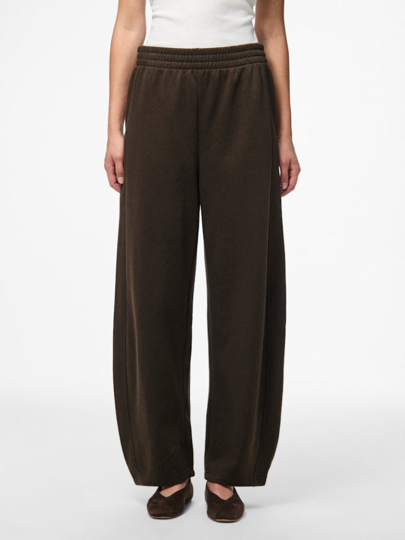 Brown barrel leg pants worn by a person on a white background