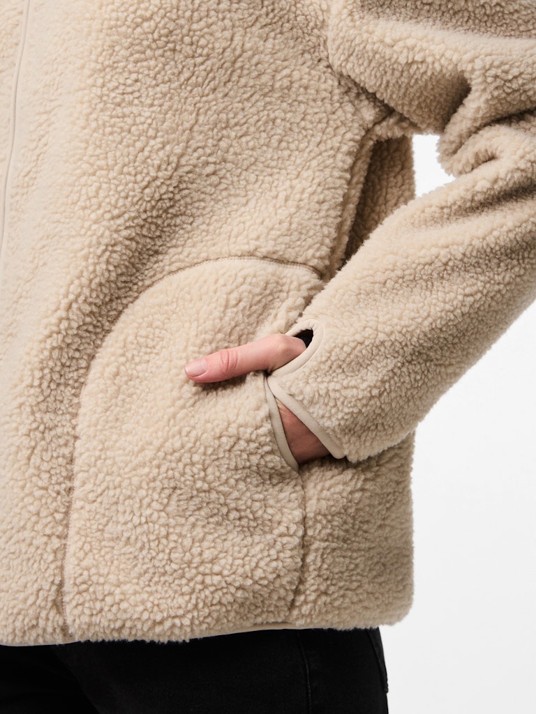Close-up of a person wearing a beige sherpa jacket with a hand in one of the pockets.