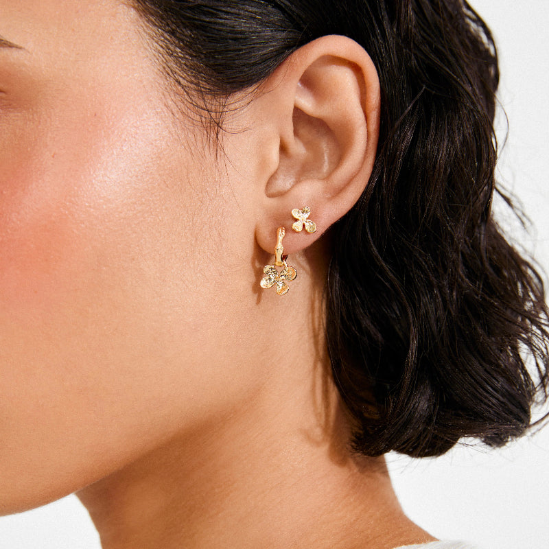 Close-up of a person wearing gold floral earrings with a neutral background