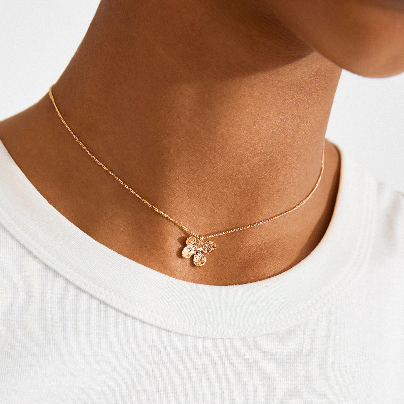 Gold necklace with a flower pendant worn by a person on a white background