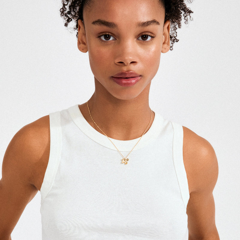 Woman wearing a white tank top and gold necklace on a plain background