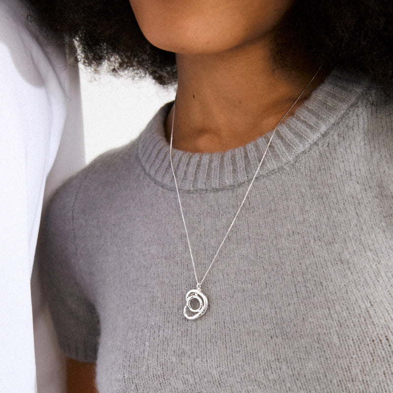 Person wearing a silver necklace with a pendant against a neutral background