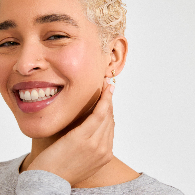 Woman with a smile, wearing a gold earring, on a plain background