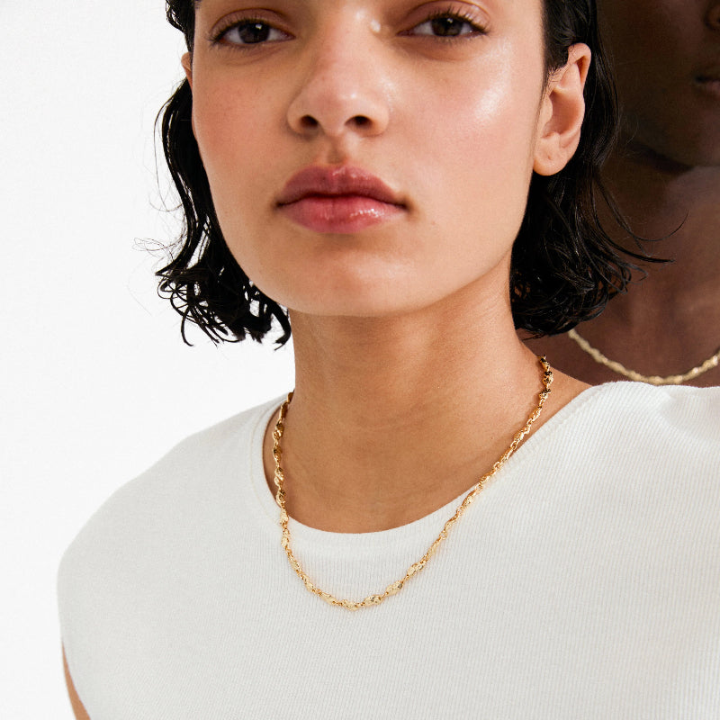 Close-up of a person wearing a gold necklace on a plain background
