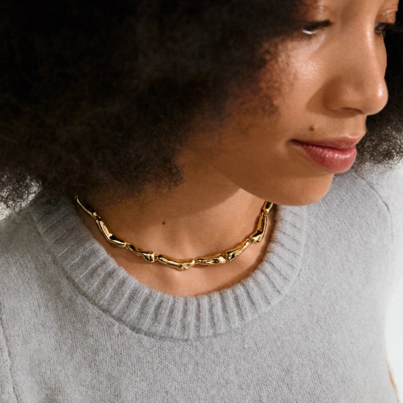Woman wearing a gold chain necklace with a gray sweater