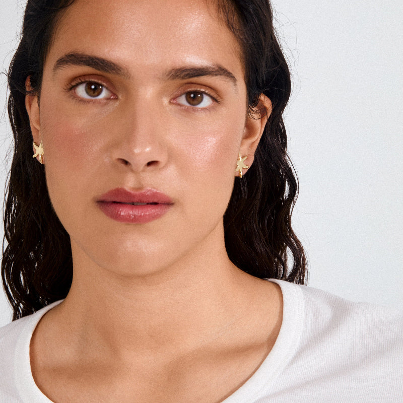 Close-up of a woman wearing gold earrings with a plain background