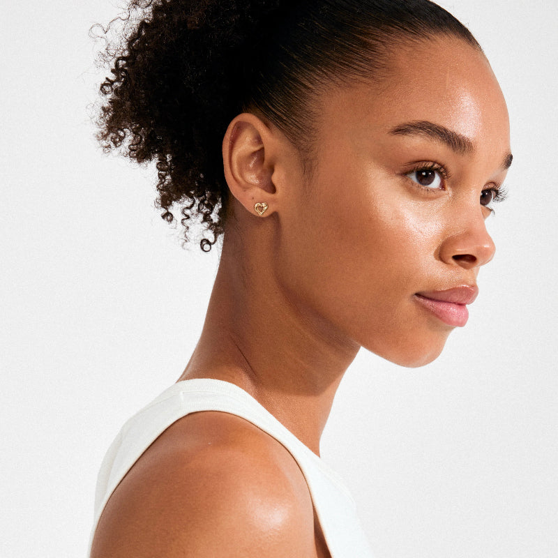 Woman wearing a gold earring and a white sleeveless top against a light background